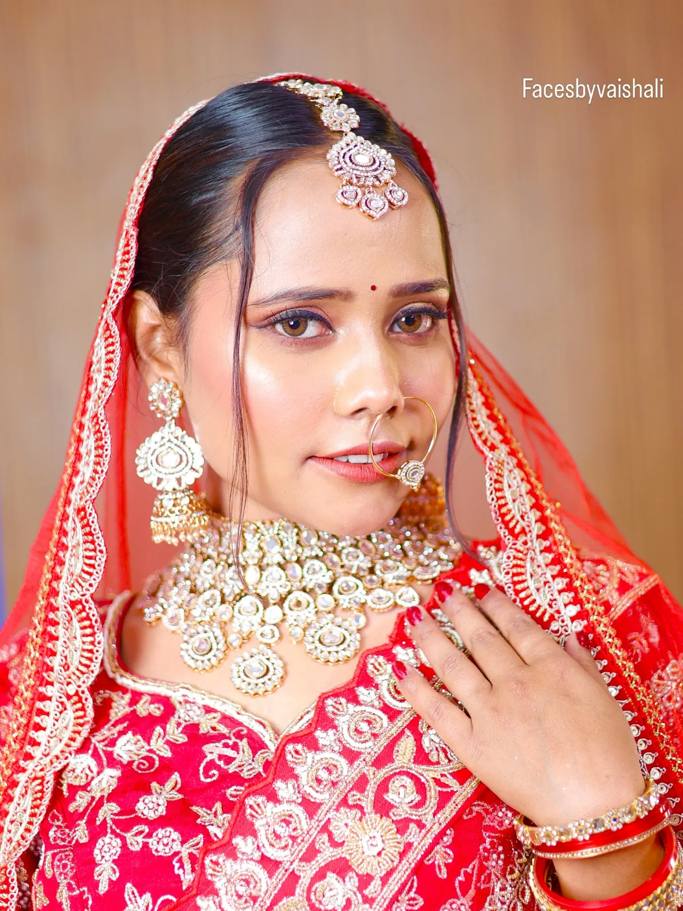 Bride in a red lehenga and dupatta with a kundan choker and maang tikka, soft glam bridal makeup