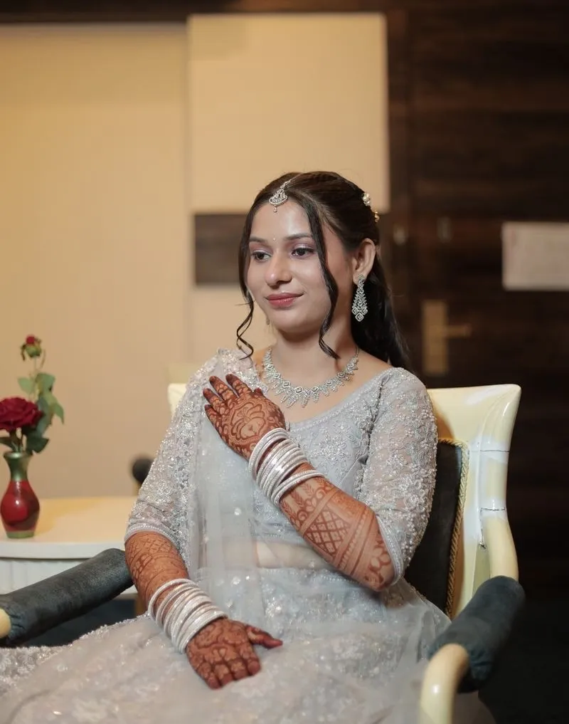 Bride in a pale silver lehenga with bridal mehendi, wearing dewy soft-glam makeup