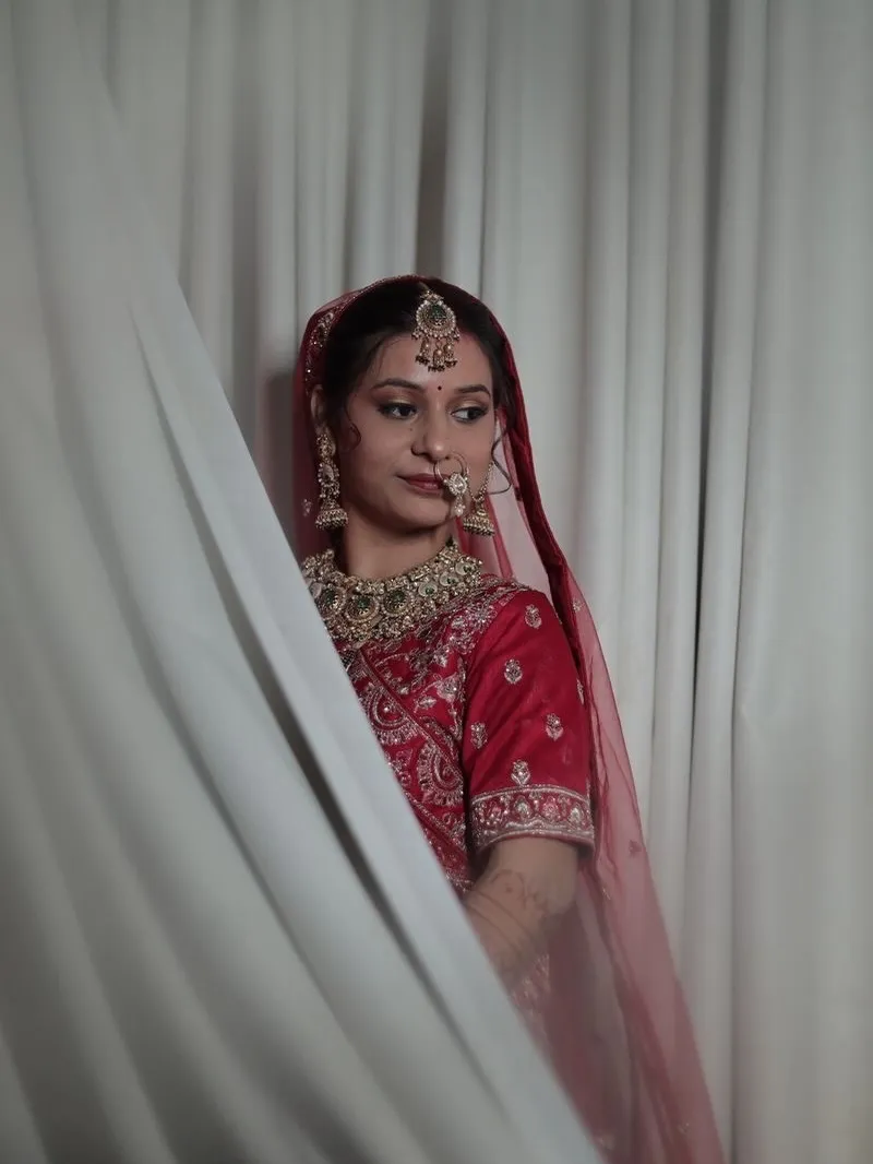 Bride in red framed by a sheer white drape, with classic red-lip bridal makeup
